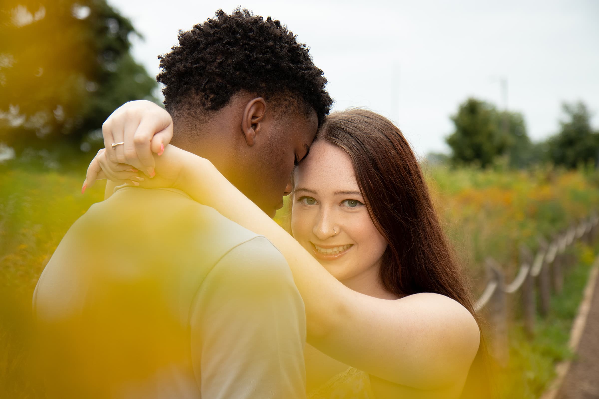Couple sharing a close embrace among yellow wildflowers during an intimate outdoor portrait photography session.