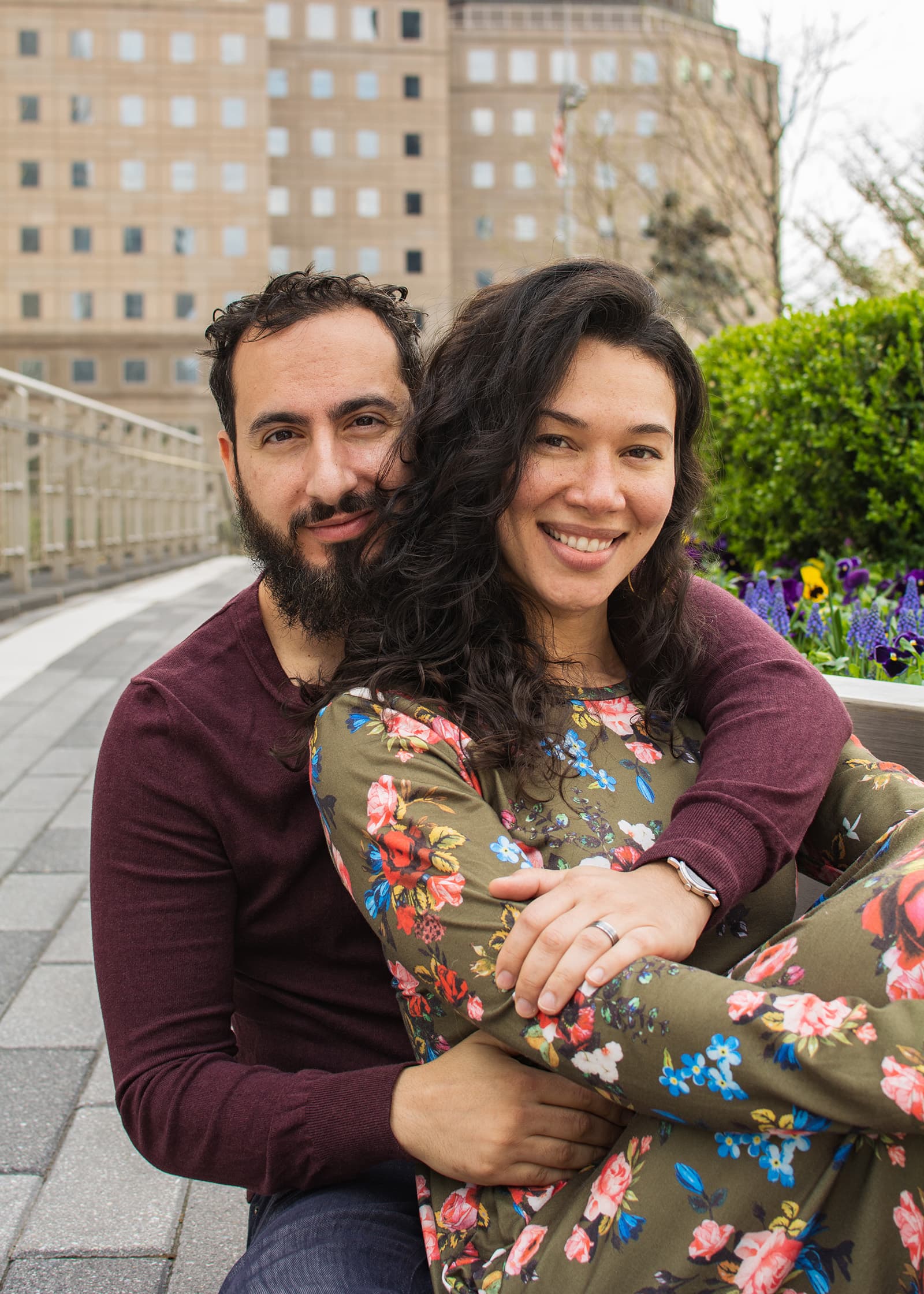 Couple holding each other and smiling during a natural outdoor portrait session in Tampa Bay beside a colorful garden.