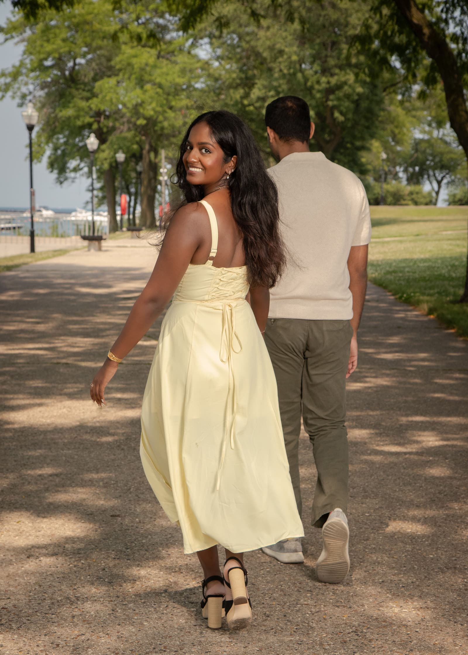 Woman looking back and smiling while walking with her partner along a shaded park path during a relaxed couples session.