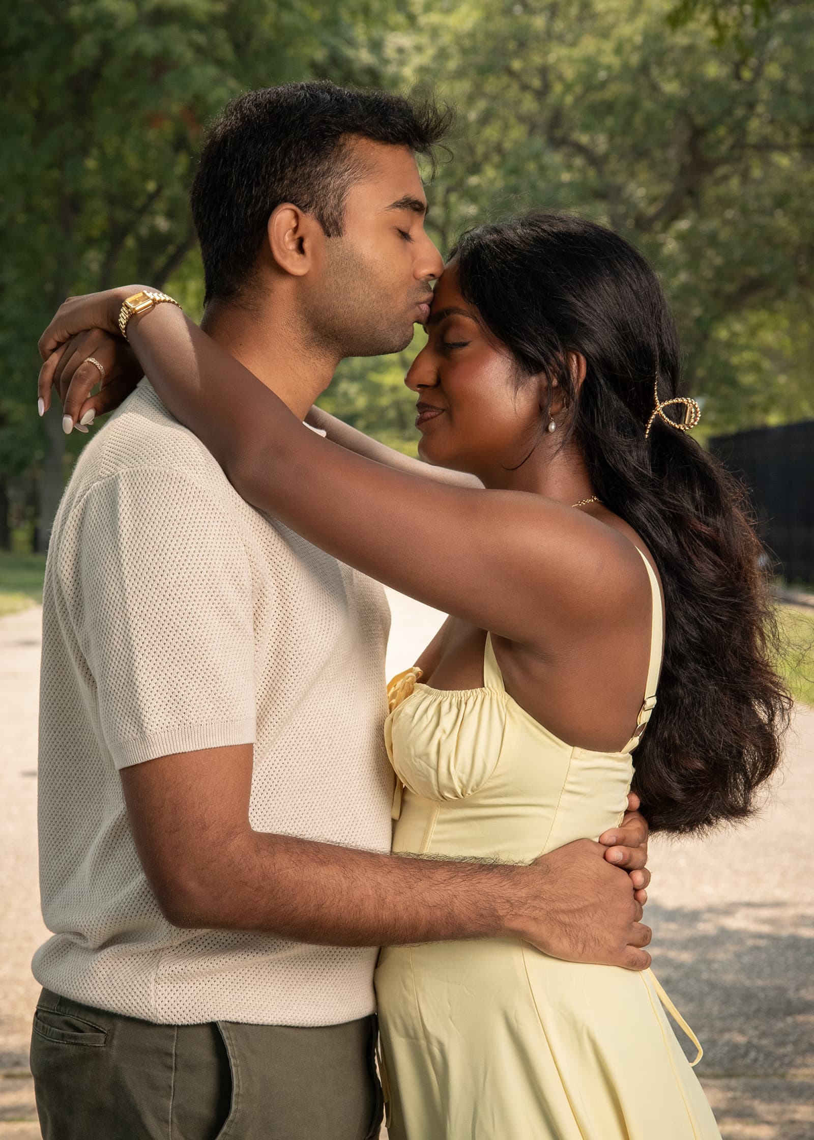 Couple sharing a tender forehead kiss during a warm outdoor portrait session surrounded by soft greenery in Tampa Bay.
