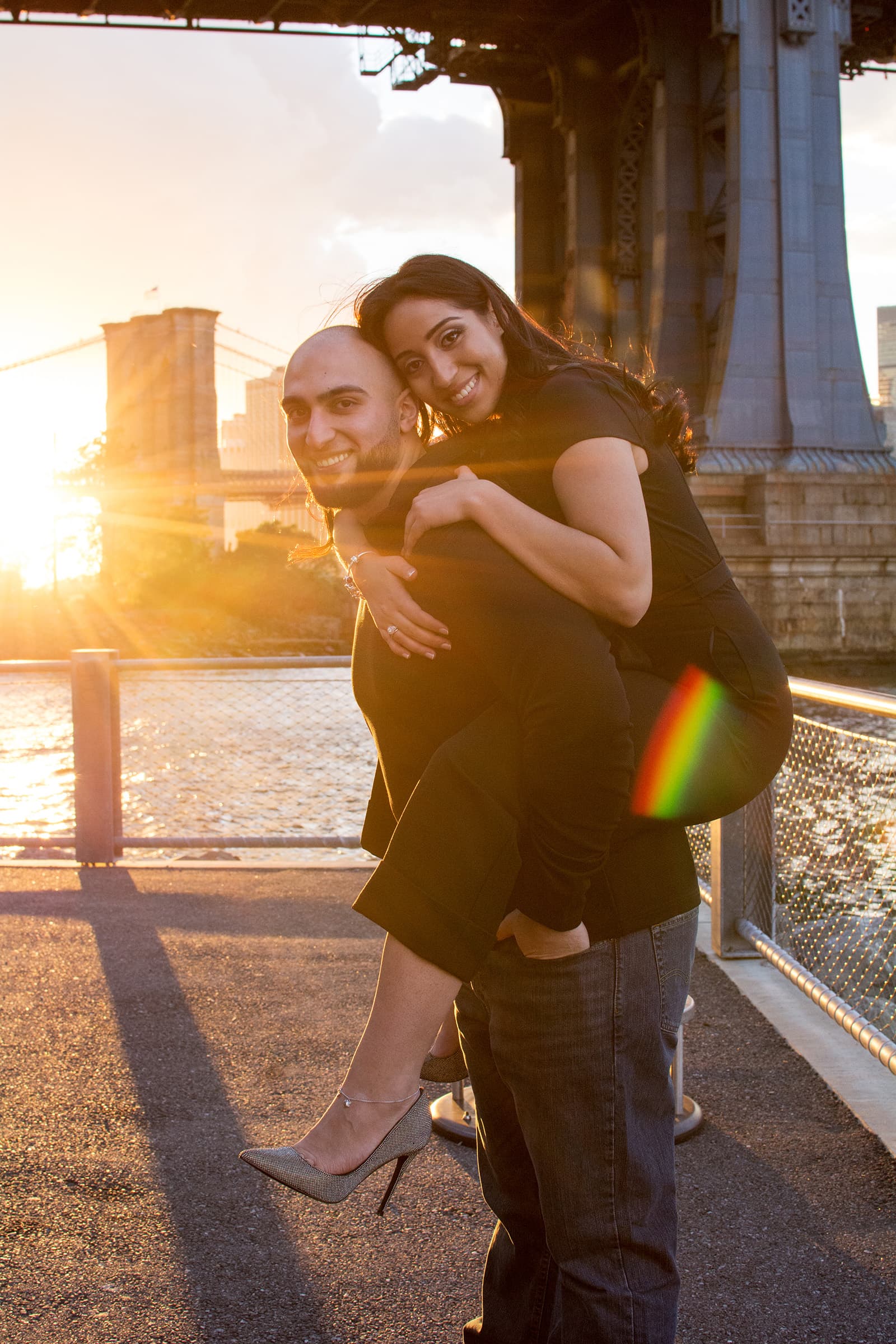 Smiling couple sharing a playful piggyback moment during a warm sunset couples portrait session with an urban backdrop.