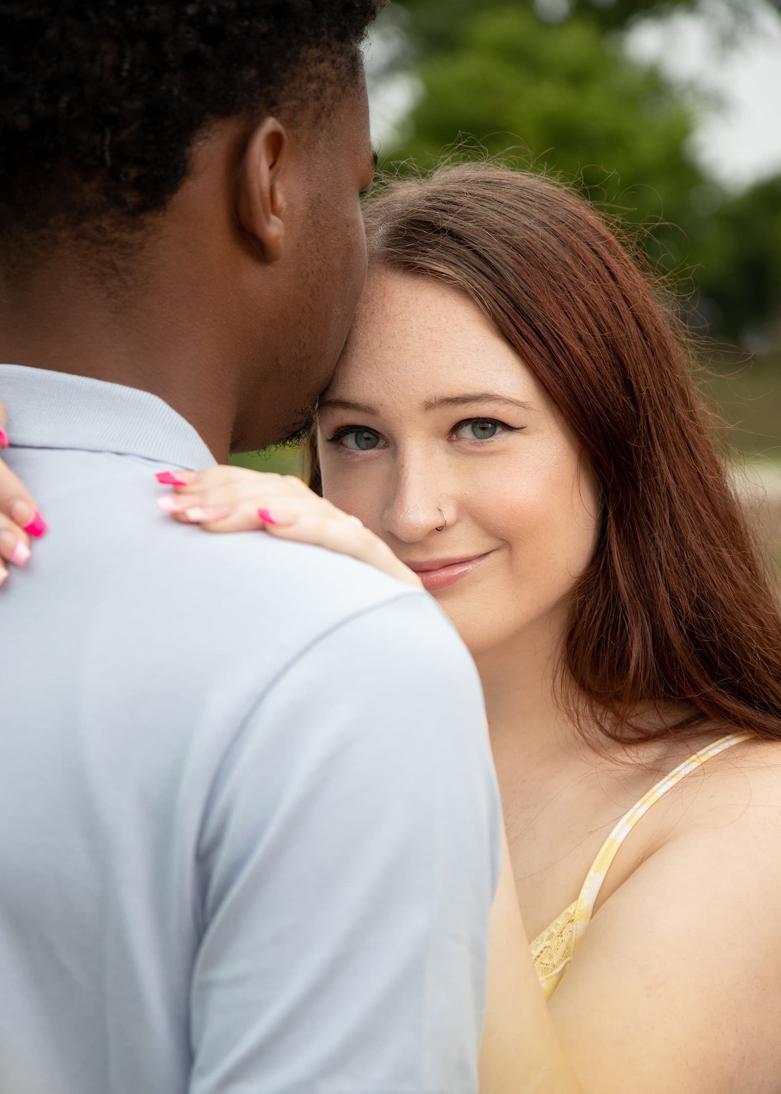 Close-up portrait of a woman smiling over her partner’s shoulder during an intimate outdoor couples photography session.