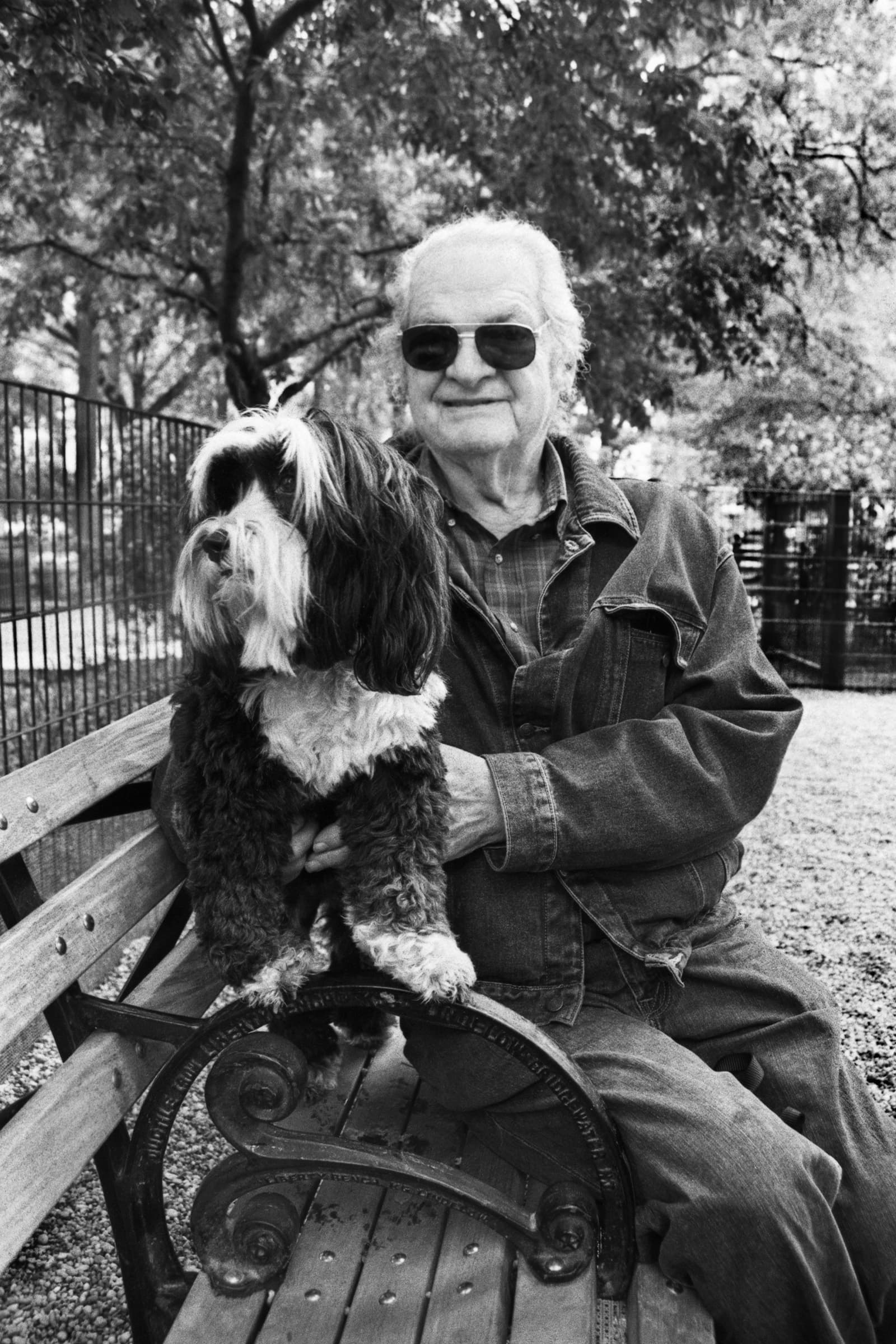 Older man holds his long-haired dog on a park bench in a candid black-and-white portrait by a Tampa Bay pet photographer.