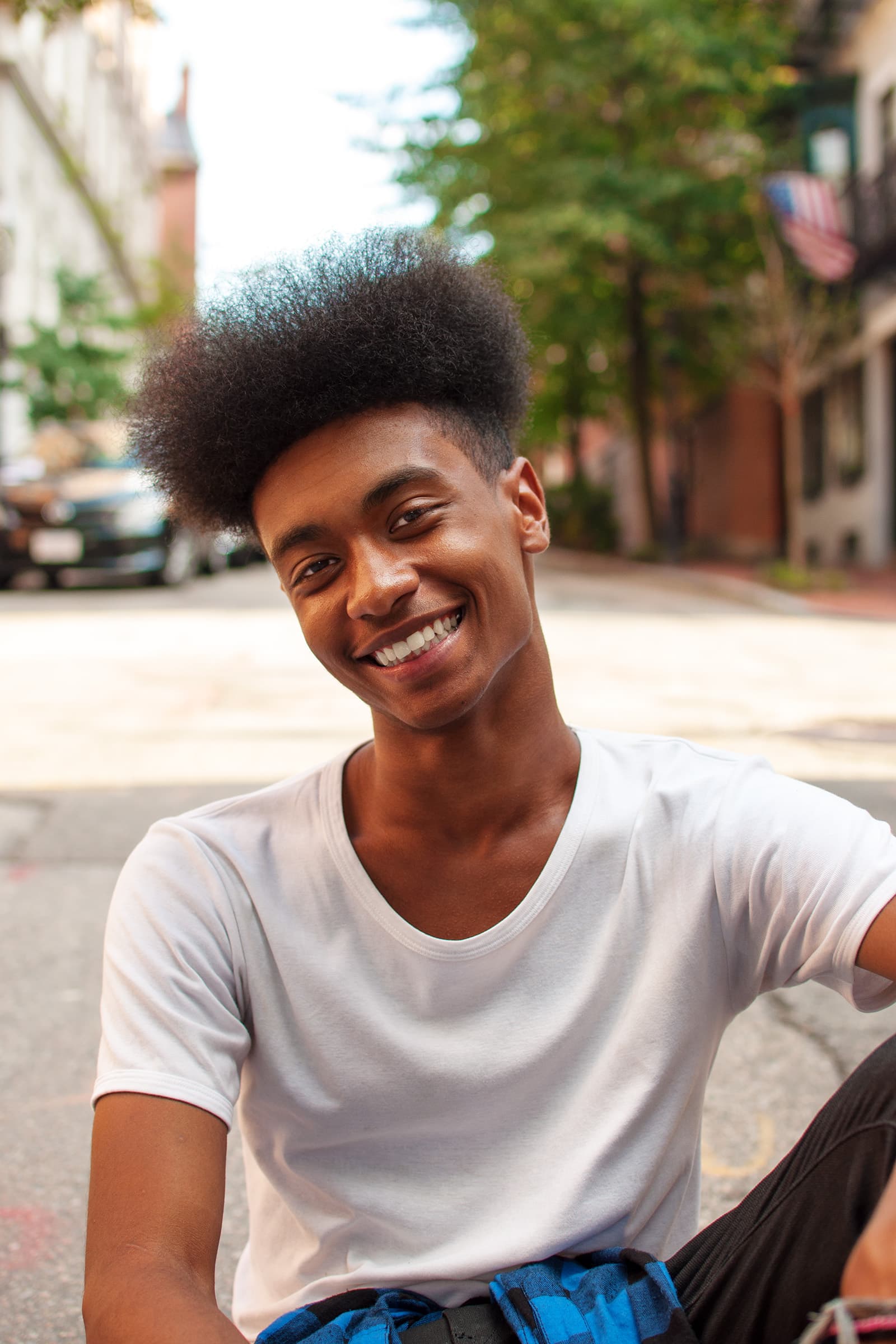 Muslims of America portrait of a smiling young Black man photographed outdoors on a quiet city street in natural light.