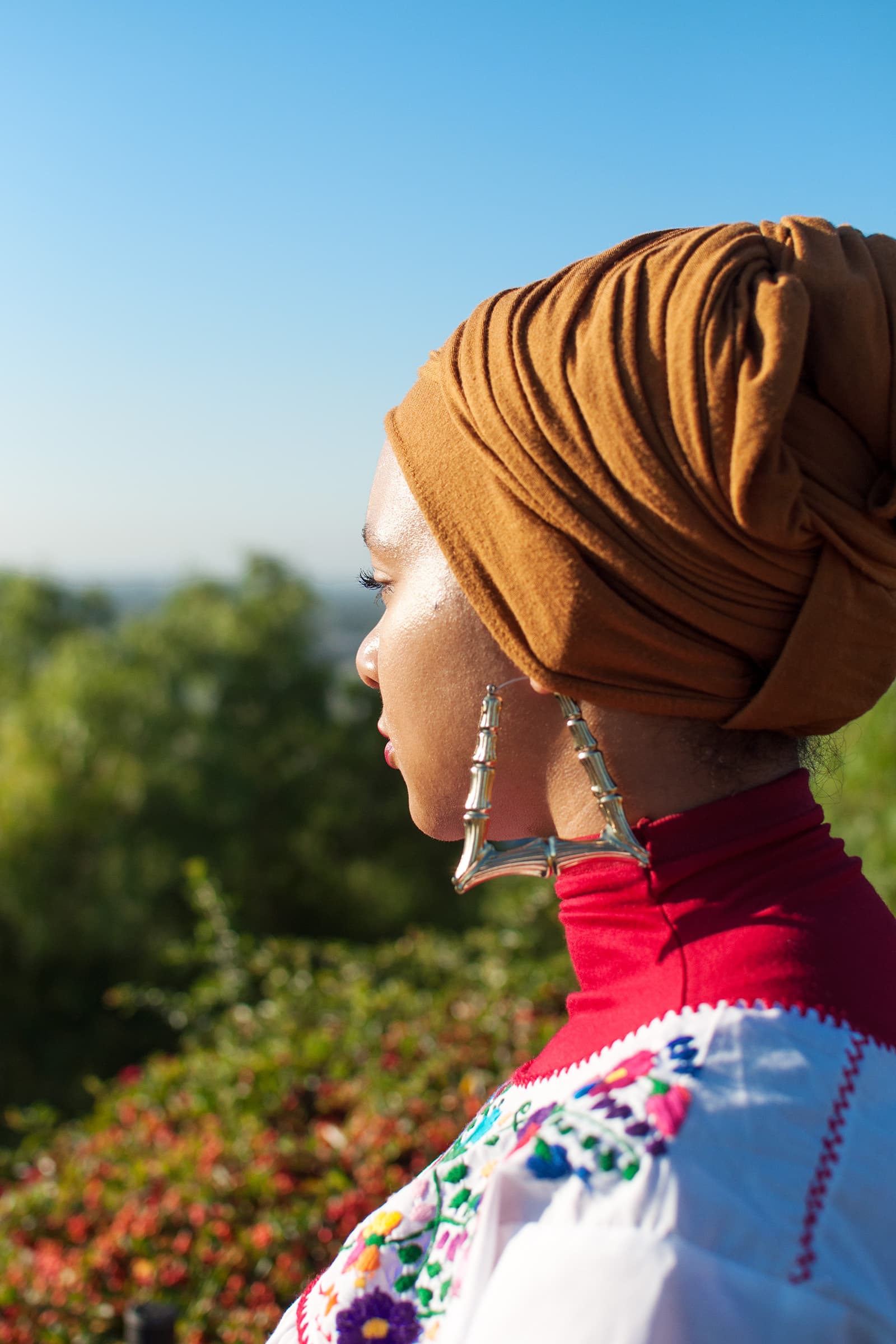 Muslims of America side-profile portrait of a Muslim woman in a brown head wrap and embroidered white top in sunlight.