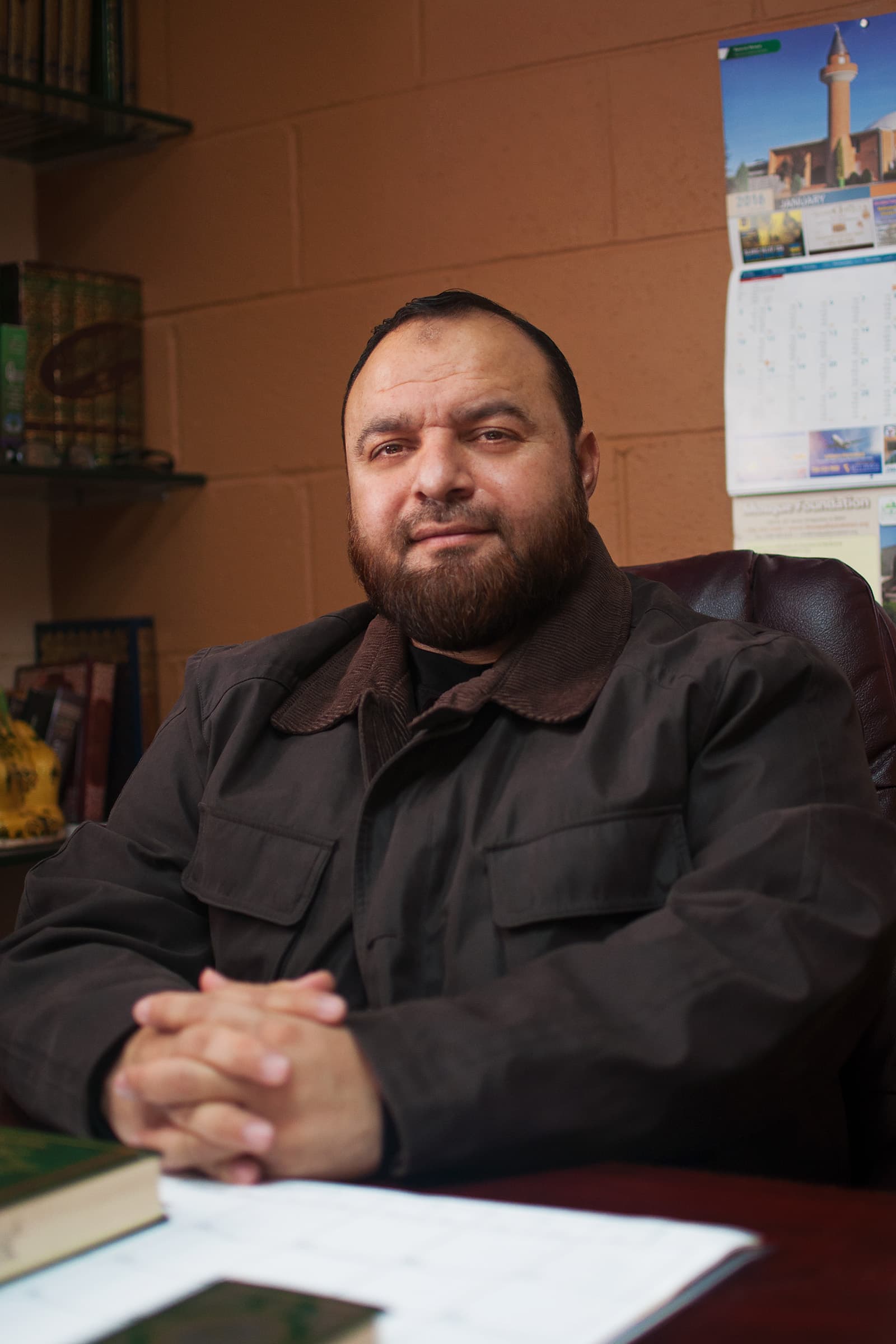 Muslims of America environmental portrait of a Muslim man with a beard seated at his desk inside a modest office.