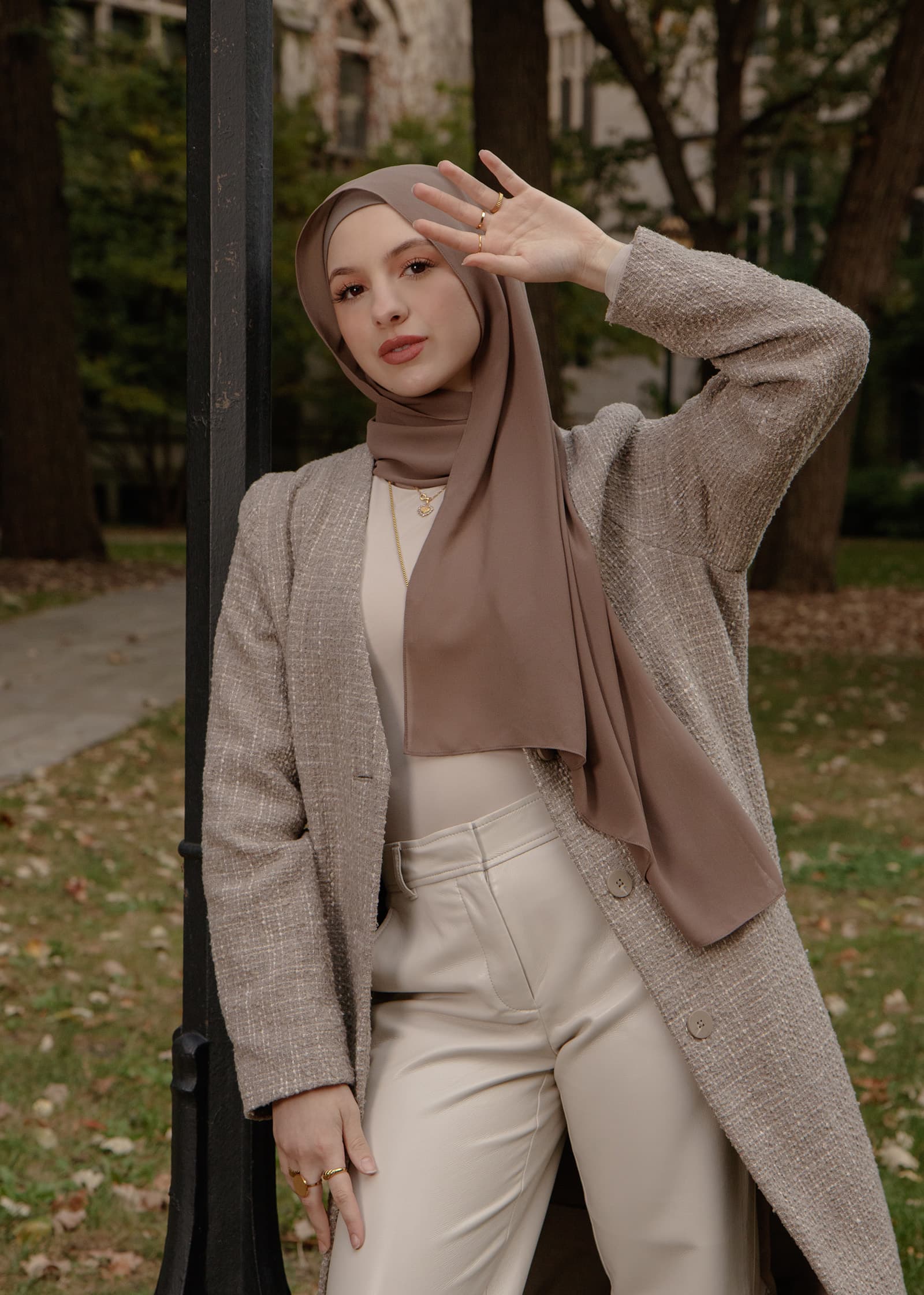 Outdoor fashion portrait of a woman in a taupe hijab, textured blazer, and cream outfit posing confidently in a park setting.