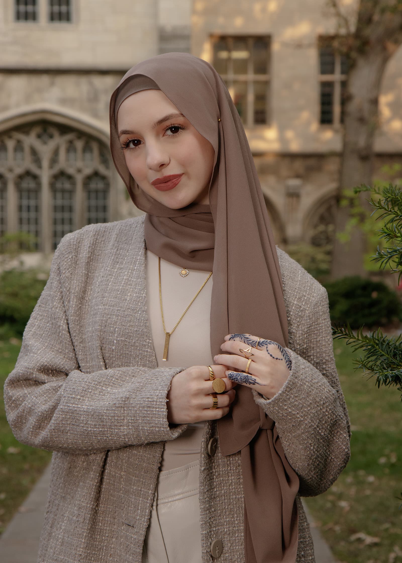Outdoor portrait of a woman in a taupe hijab and neutral blazer, photographed in soft natural light near historic buildings.