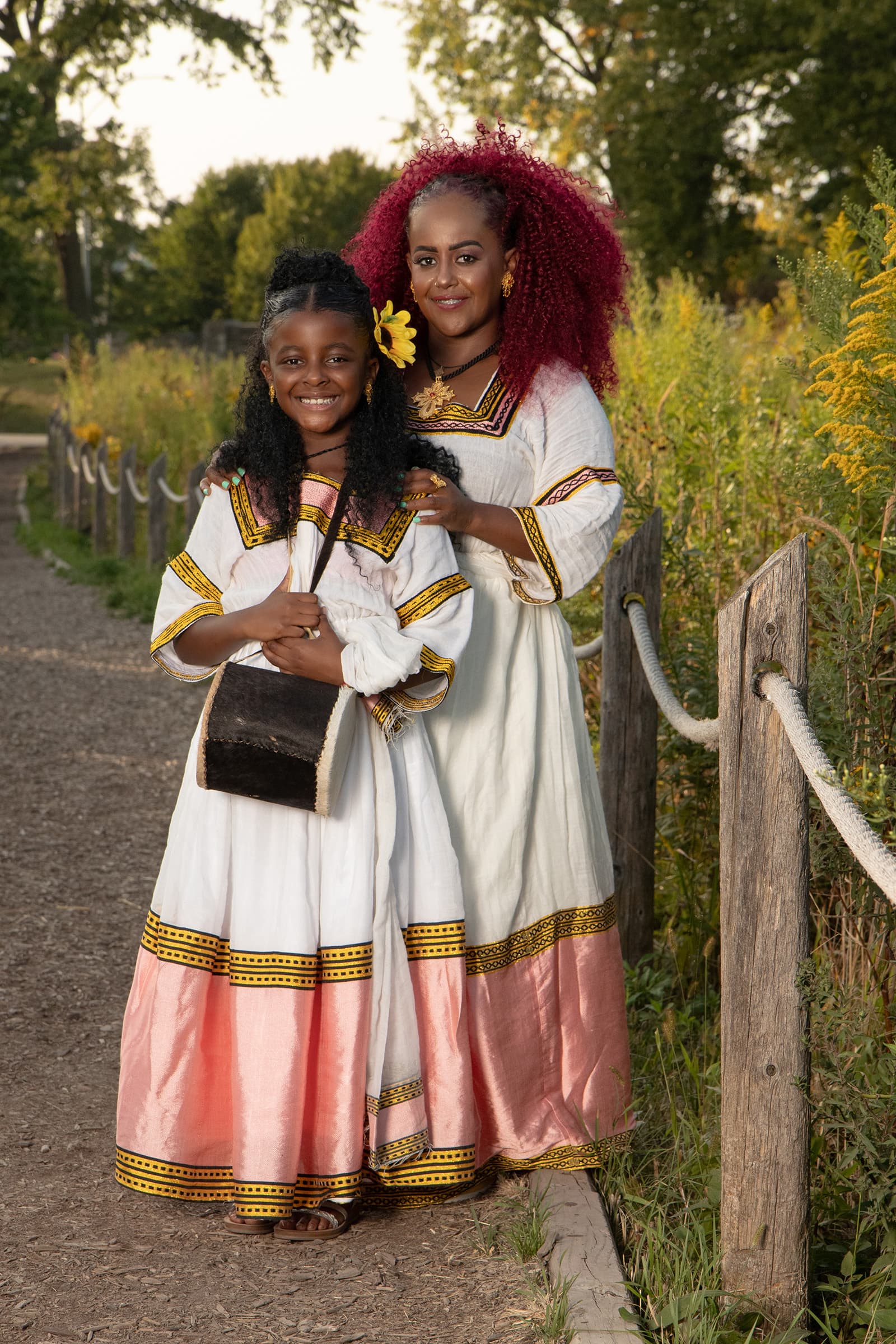 Outdoor portrait of a mother and daughter in traditional embroidered dresses, photographed together in warm natural light.
