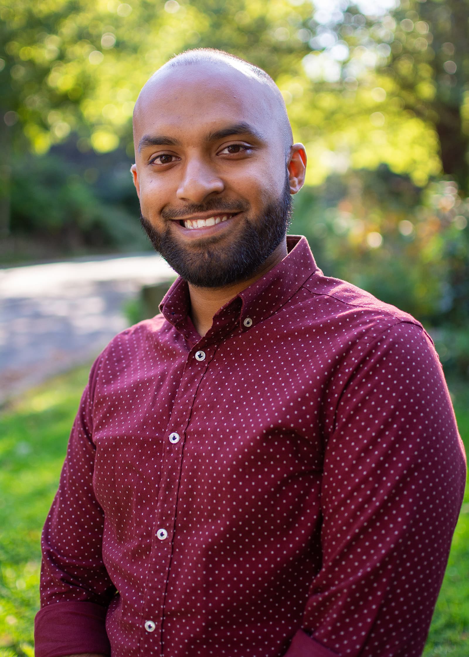 Professional outdoor headshot of a smiling man in a burgundy shirt, photographed against soft greenery in Tampa Bay.