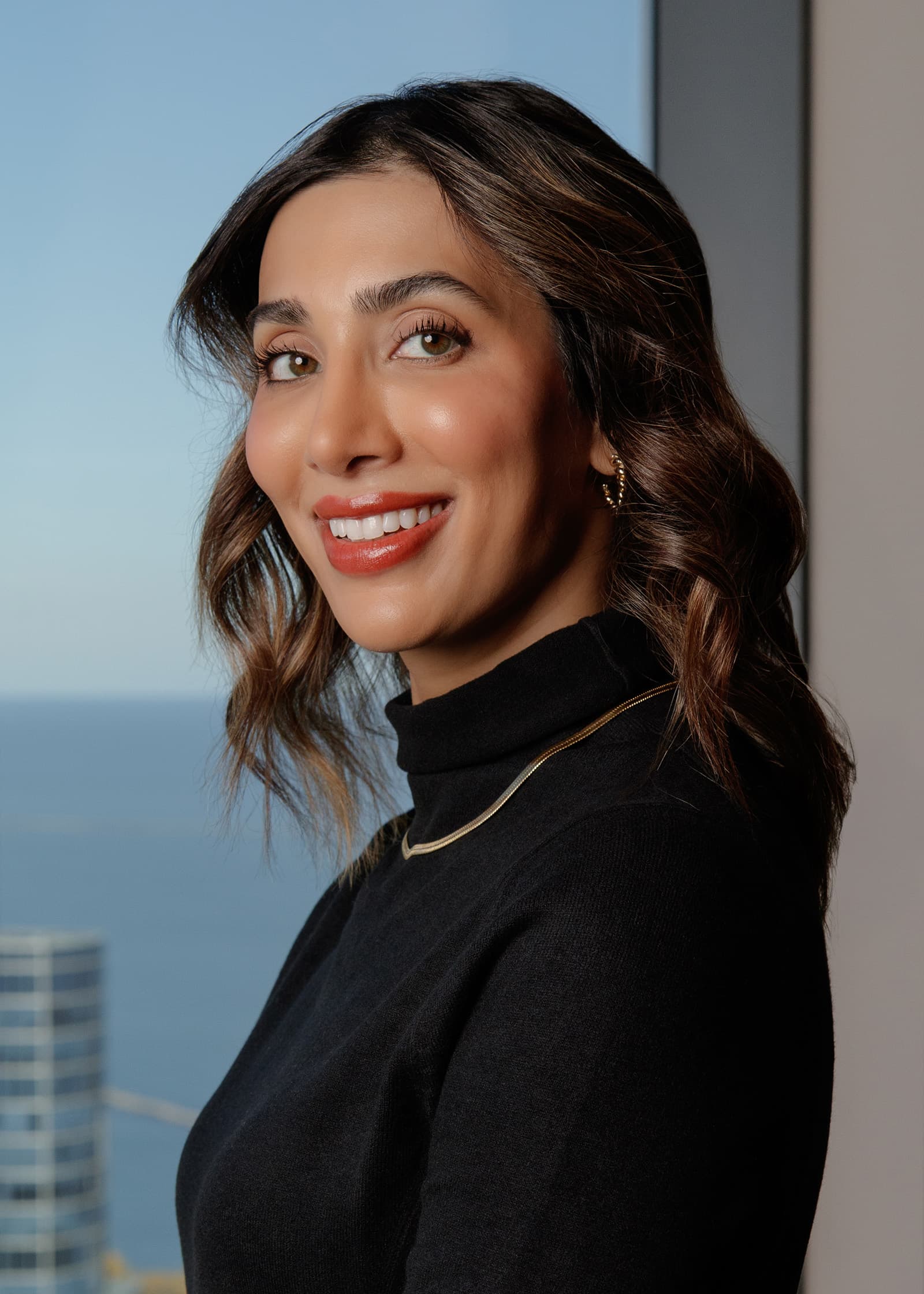 Professional headshot of a smiling woman in black photographed beside a high-rise window in Downtown Tampa.