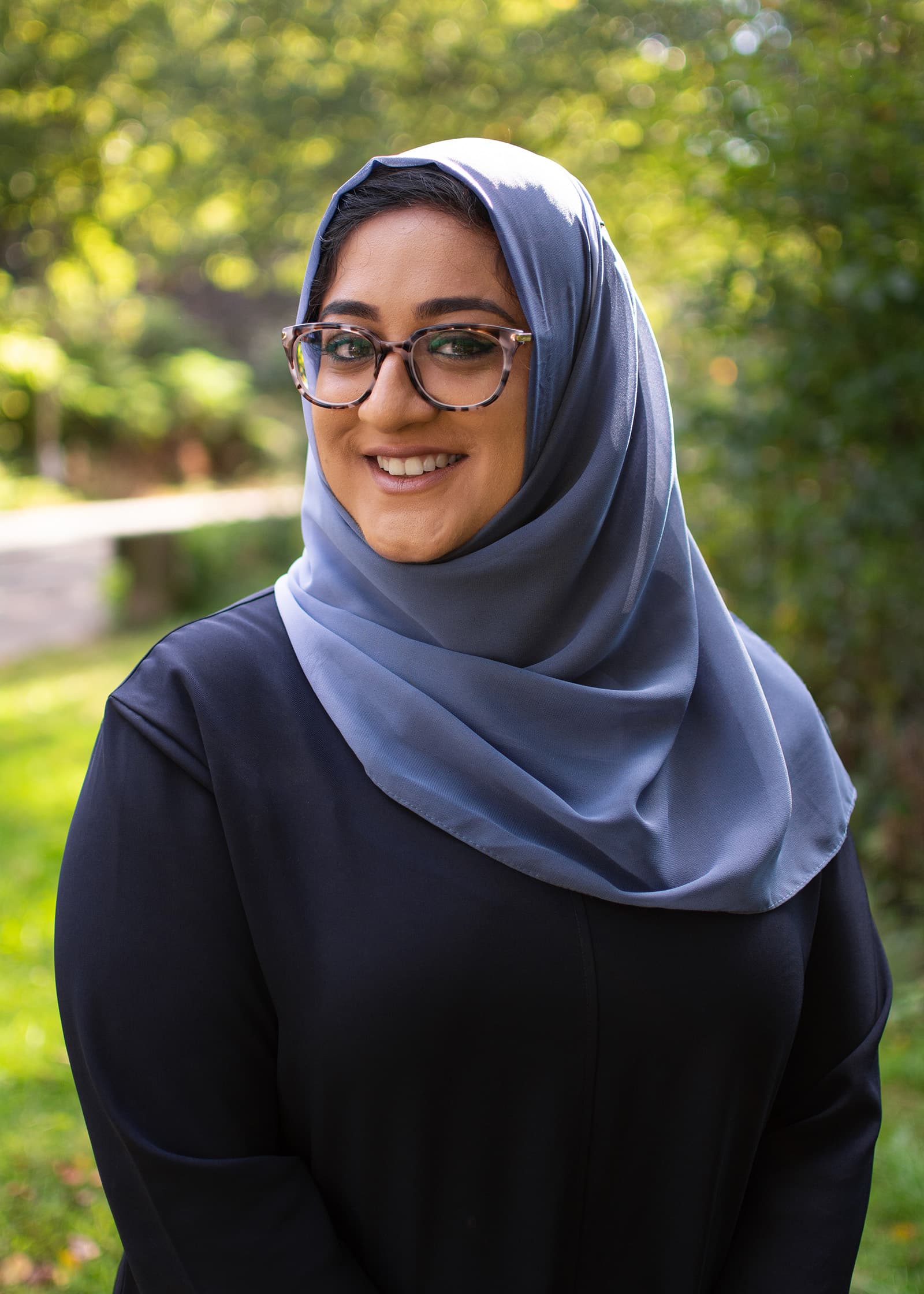 Professional outdoor portrait of a woman in a blue hijab and glasses, photographed against soft greenery in Tampa Bay.