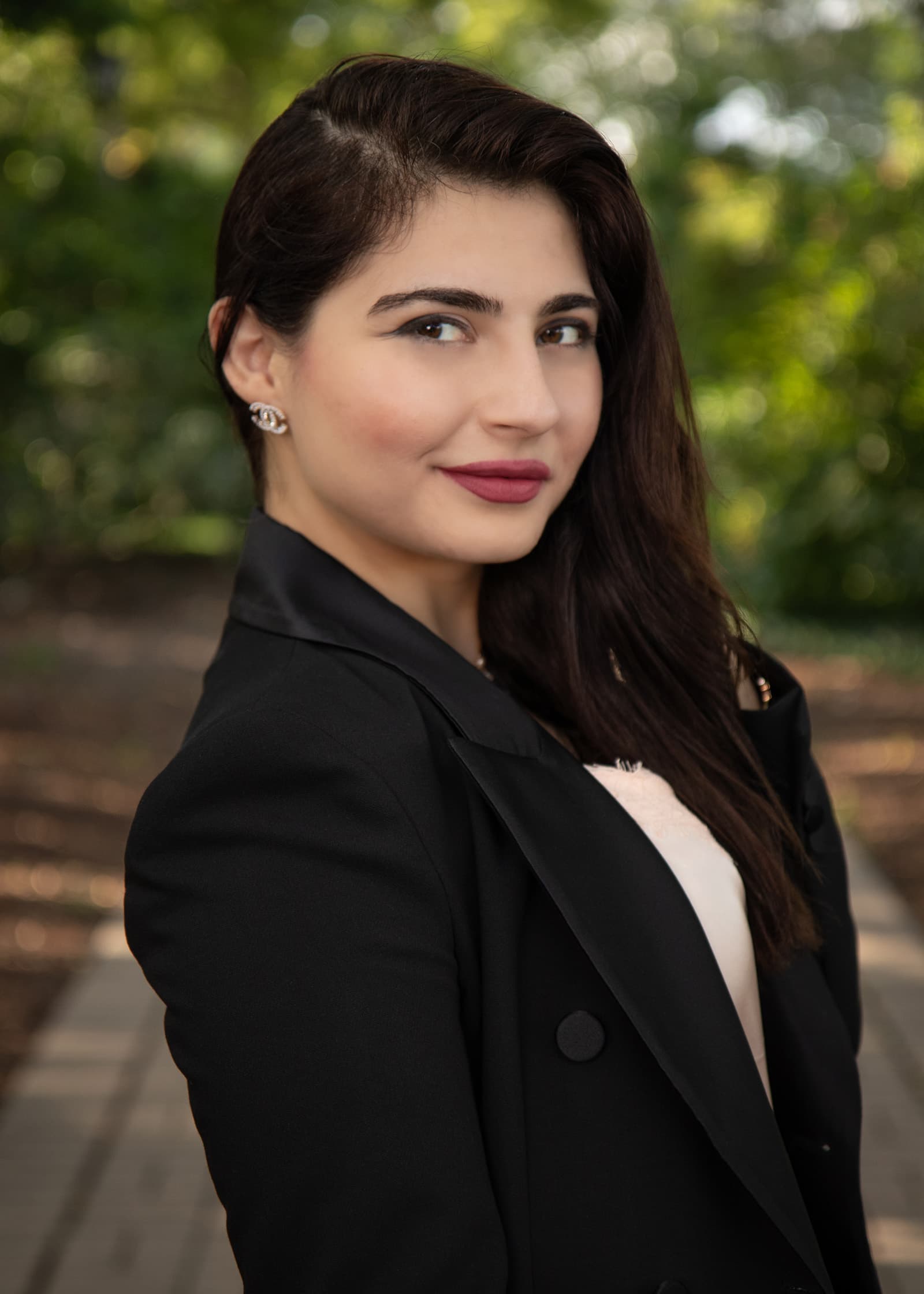 Professional outdoor headshot of a woman in a black blazer with softly blurred greenery in the Tampa Bay area.