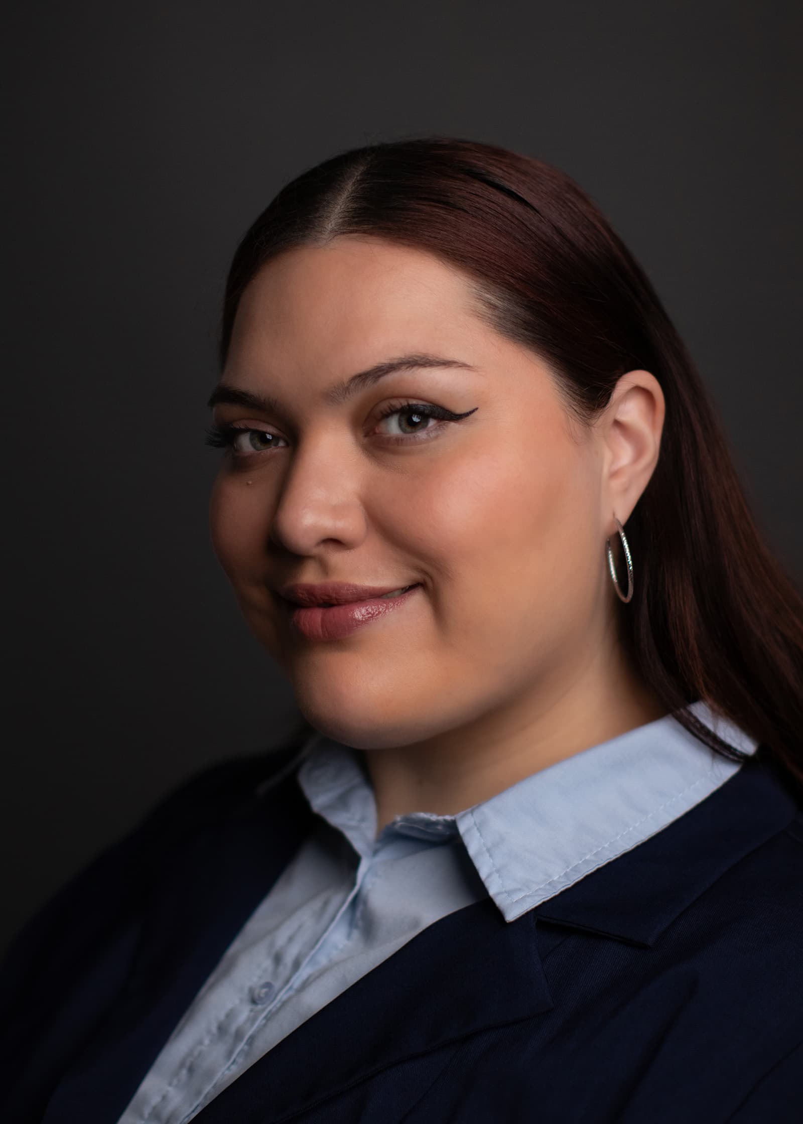 Professional studio headshot of a woman in a navy blazer and blue shirt against a dark neutral Tampa studio background.