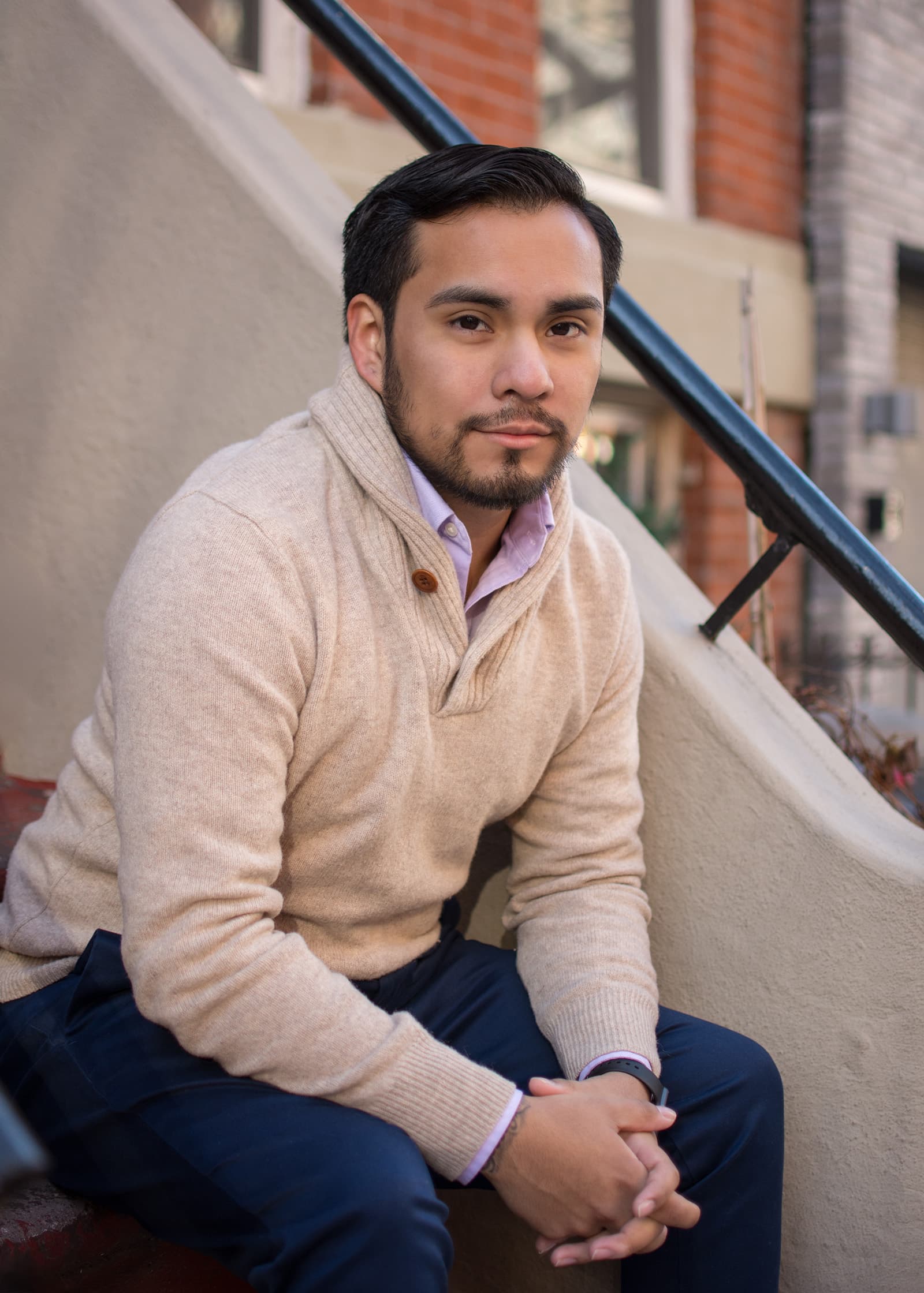 Professional portrait of a seated man in a beige sweater on urban steps, photographed in the Tampa Bay area.
