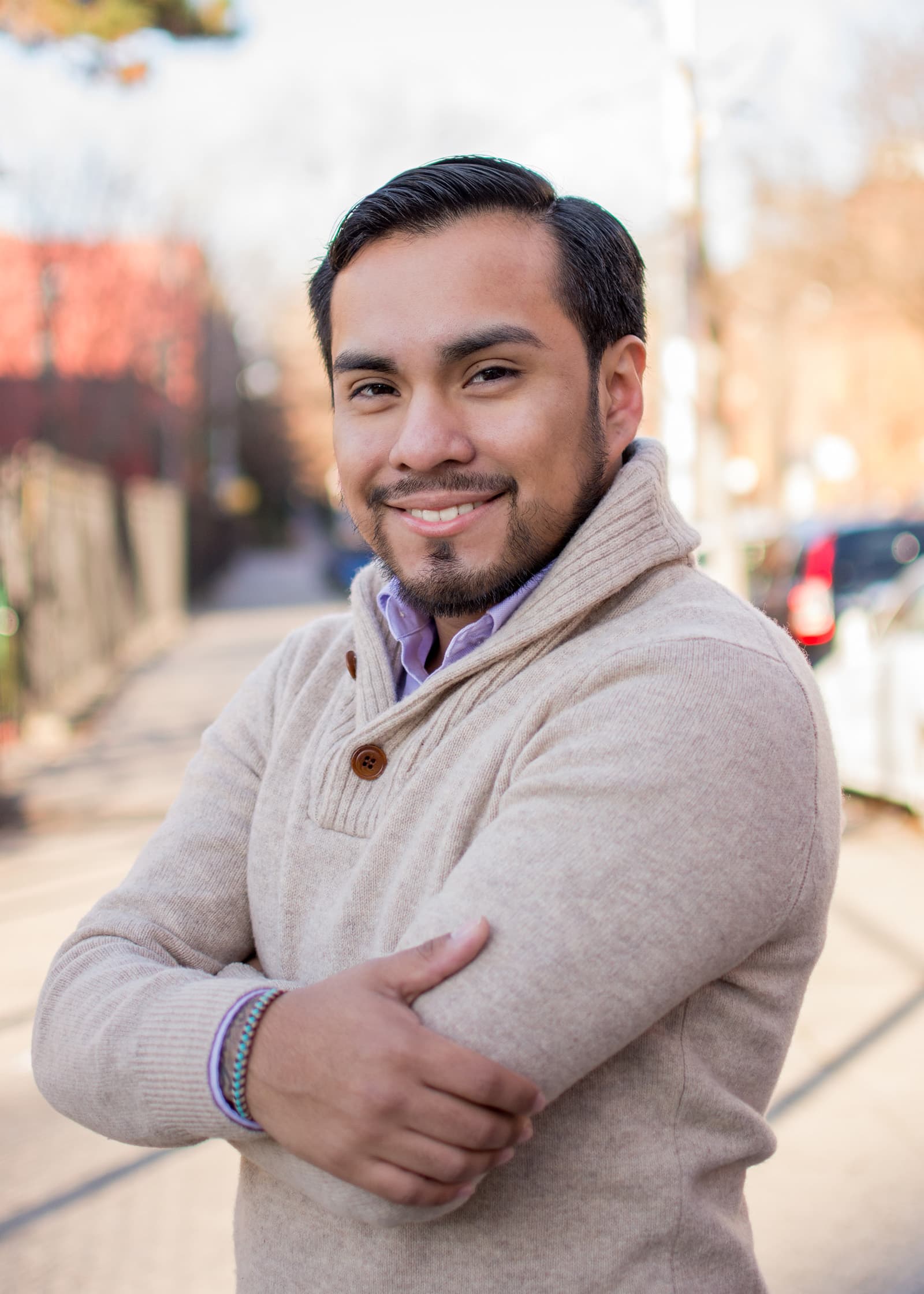 Outdoor professional headshot of a smiling man in a beige sweater with a softly blurred Tampa street behind him.