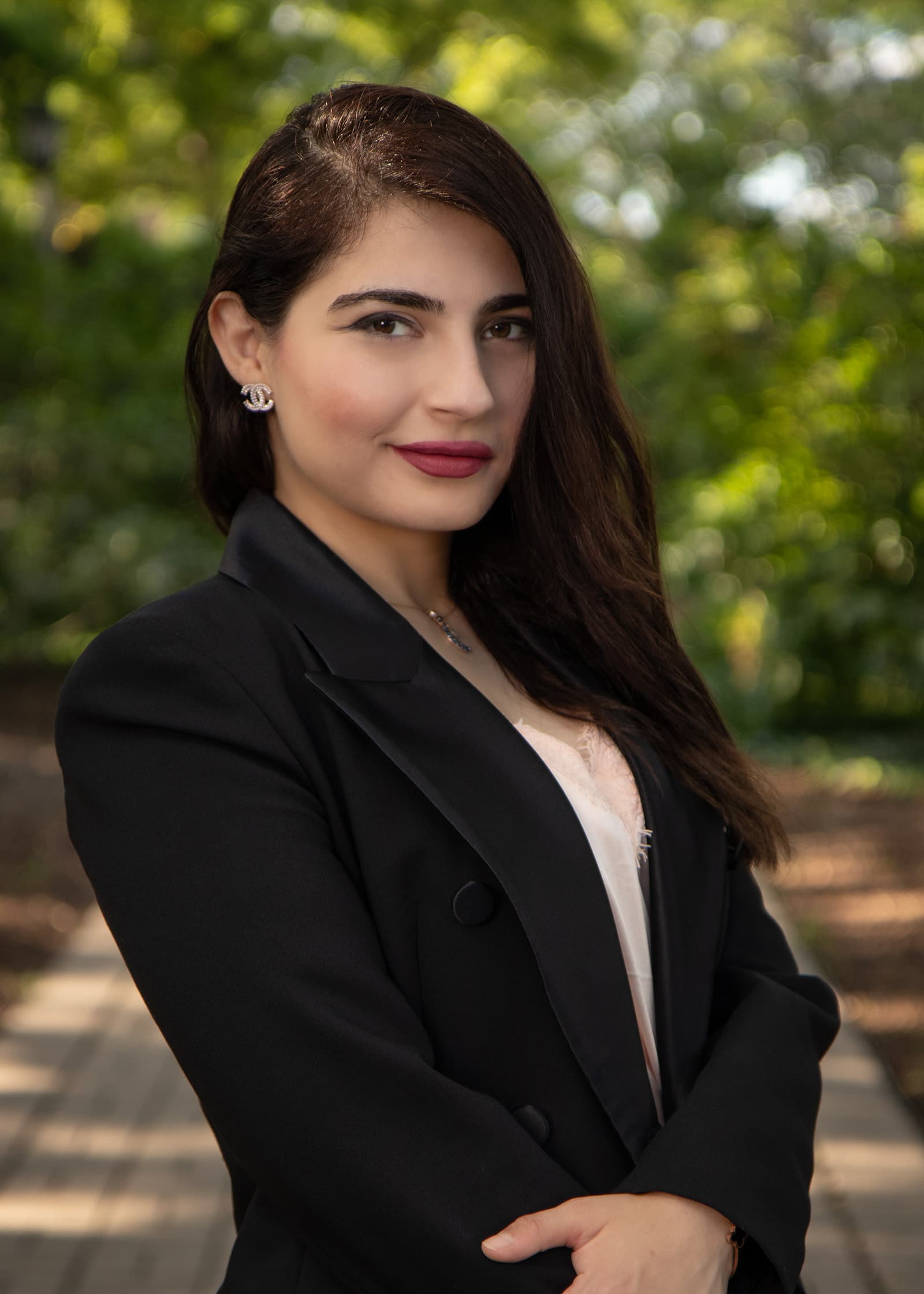 Professional outdoor portrait of a woman in a black blazer photographed against soft green foliage in Tampa Bay.