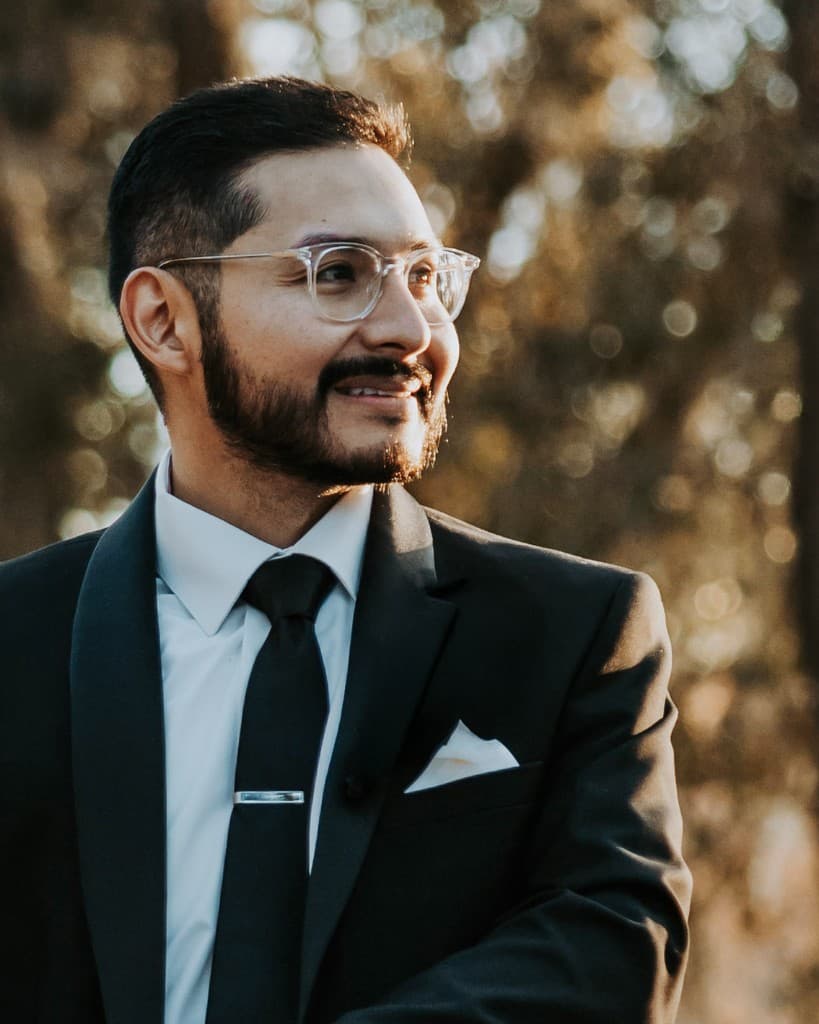 Professional headshot of a man in a dark suit with glasses, photographed outdoors by Khalil Studios in Tampa