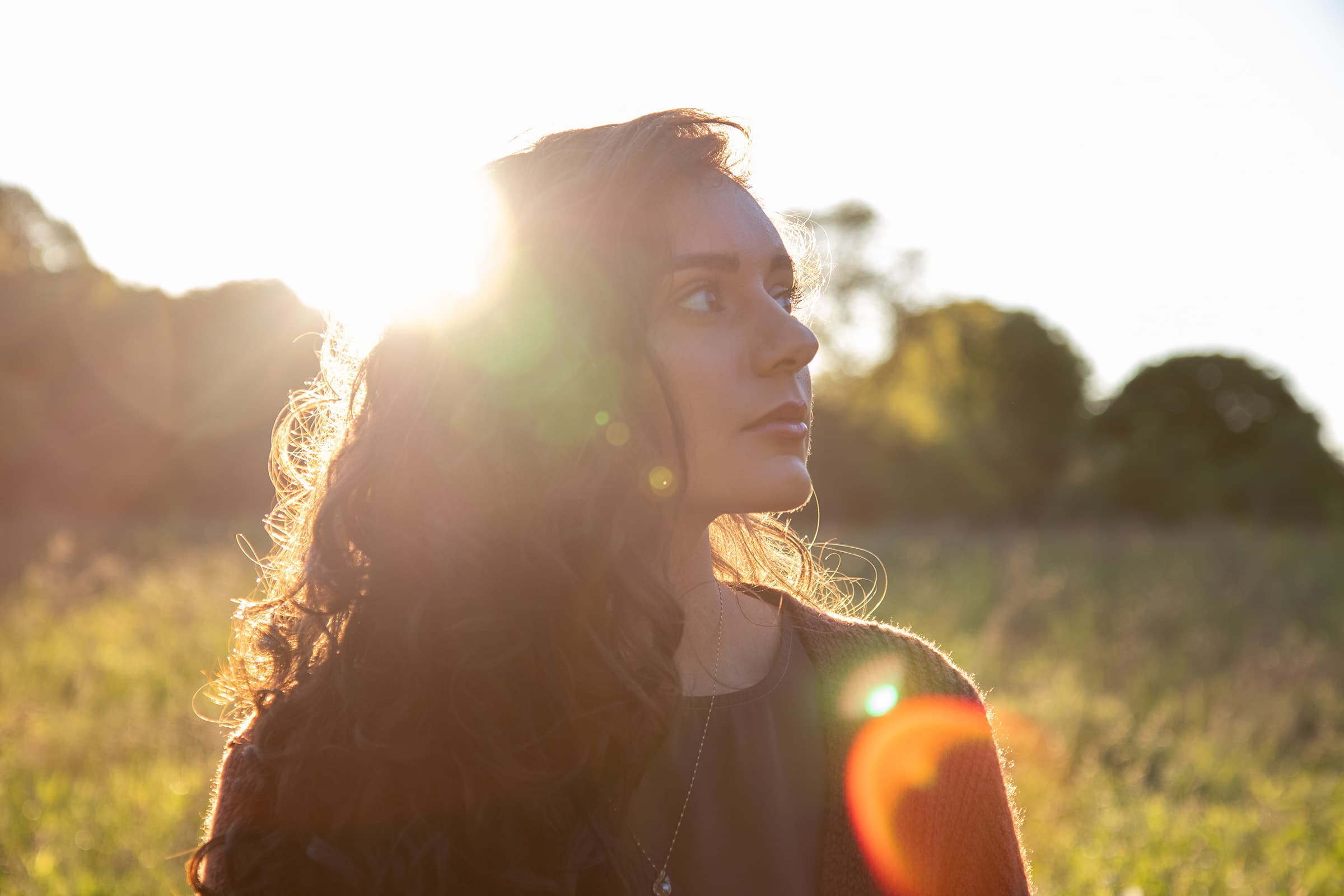 Cinematic outdoor portrait of a professional woman in Tampa, backlit by warm golden-hour sunlight with natural lens flare.