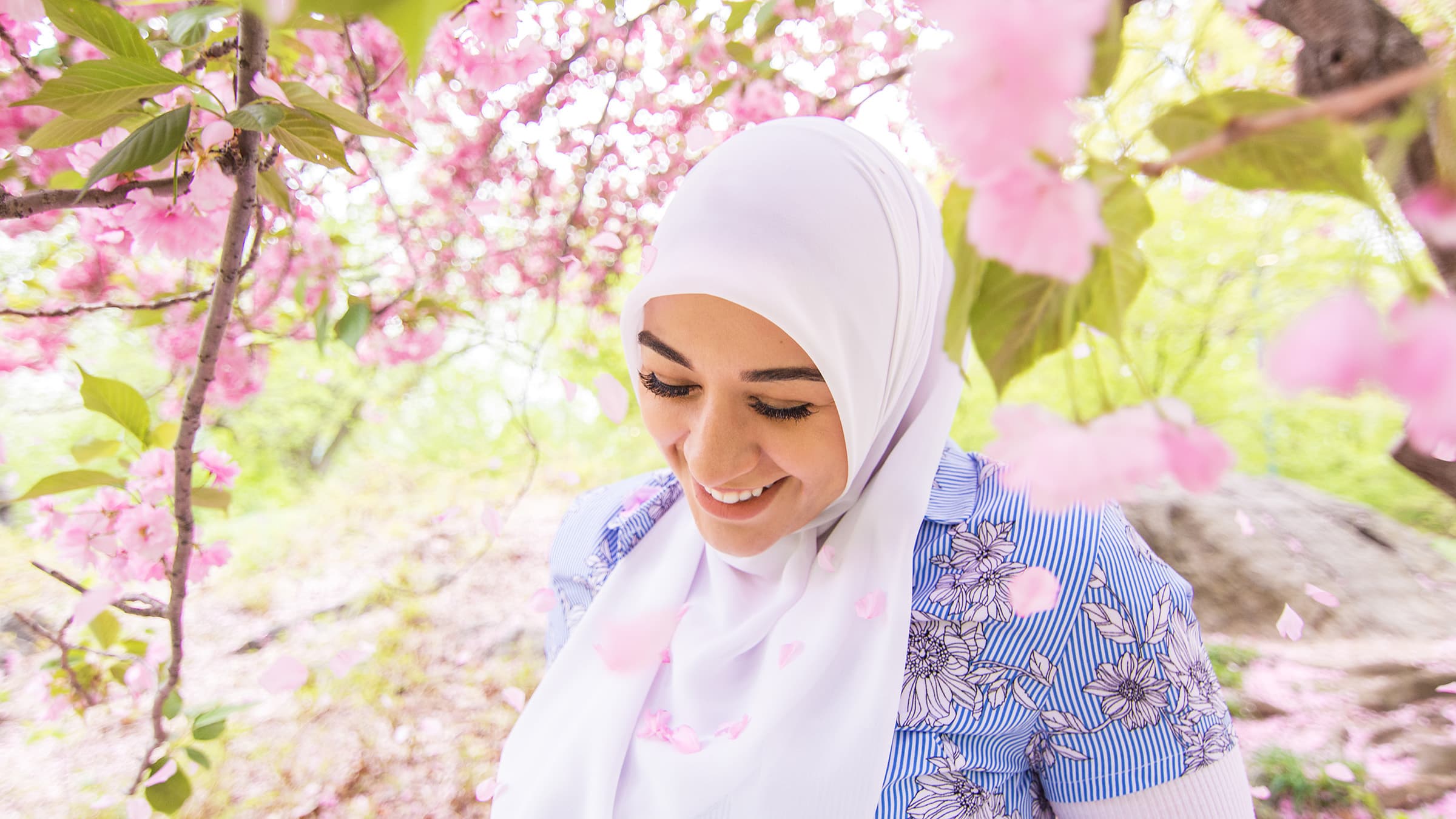 Bright outdoor portrait of a woman in a white hijab surrounded by pink spring blossoms and soft natural light in Tampa.