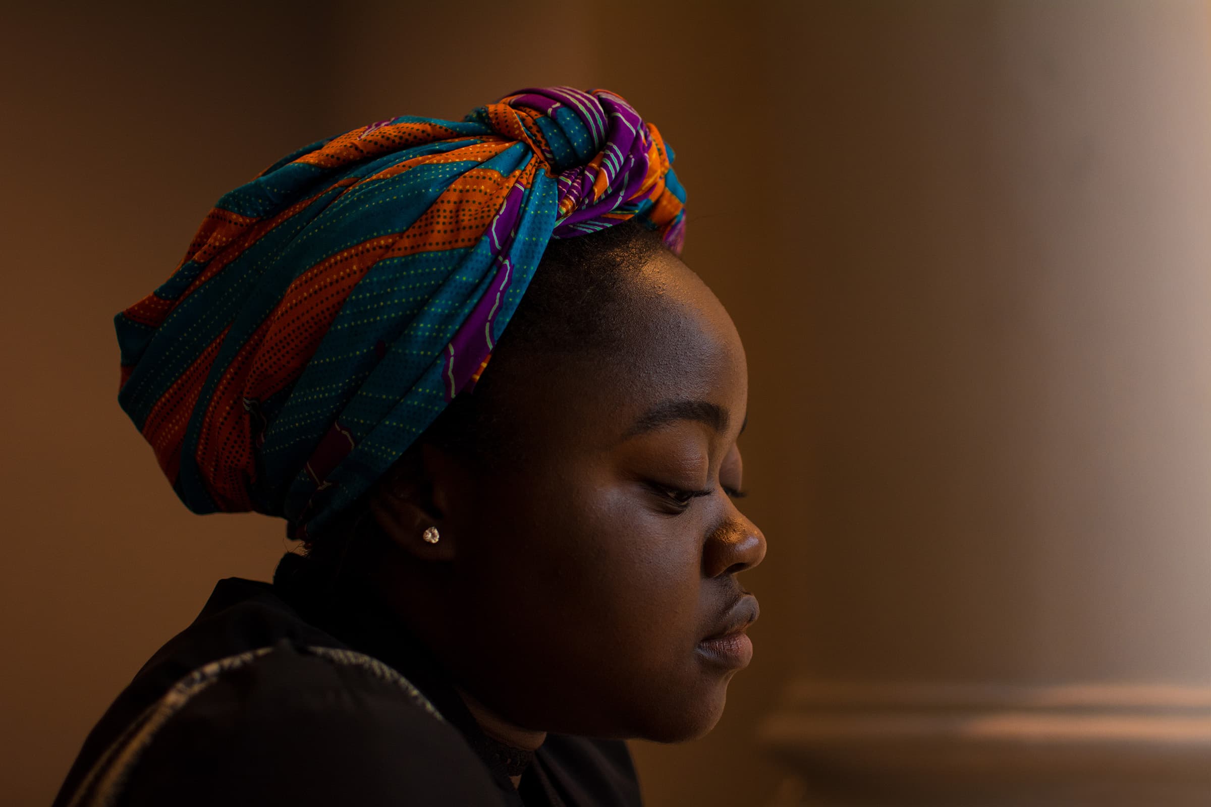 Indoor cinematic profile portrait of a woman in a colorful headwrap, photographed with soft directional natural light.