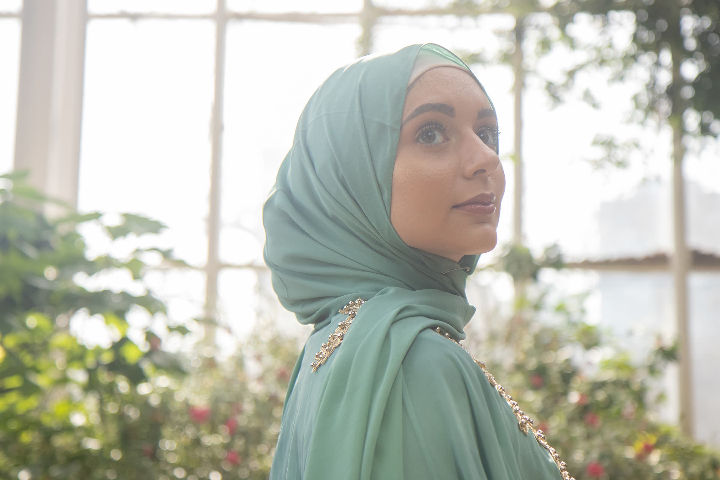 Professional portrait of a woman in a mint hijab, photographed indoors in Tampa with bright window light and soft greenery.