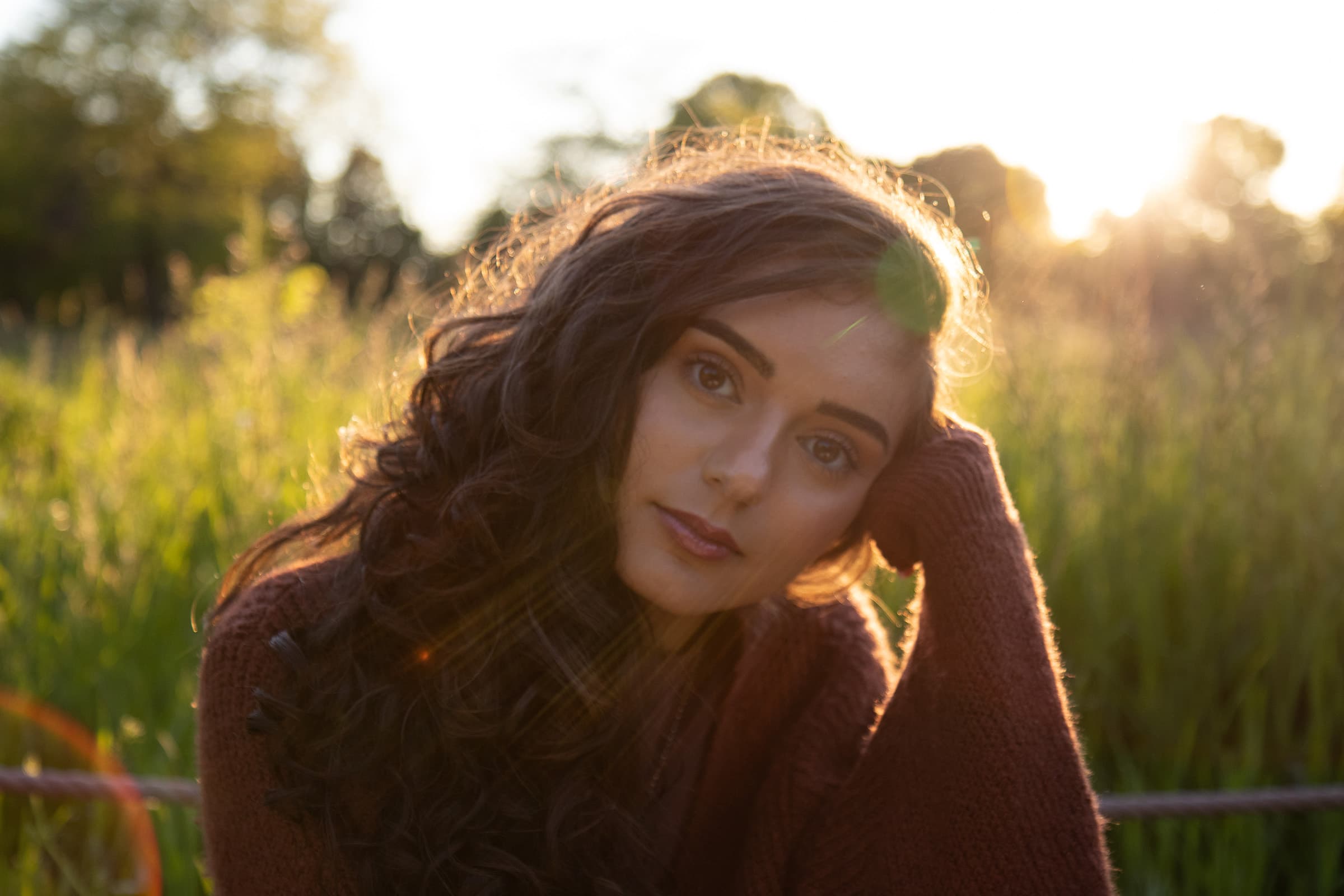 Golden-hour portrait of a professional woman in Tampa, wearing a brown sweater with warm backlight and natural lens flare.