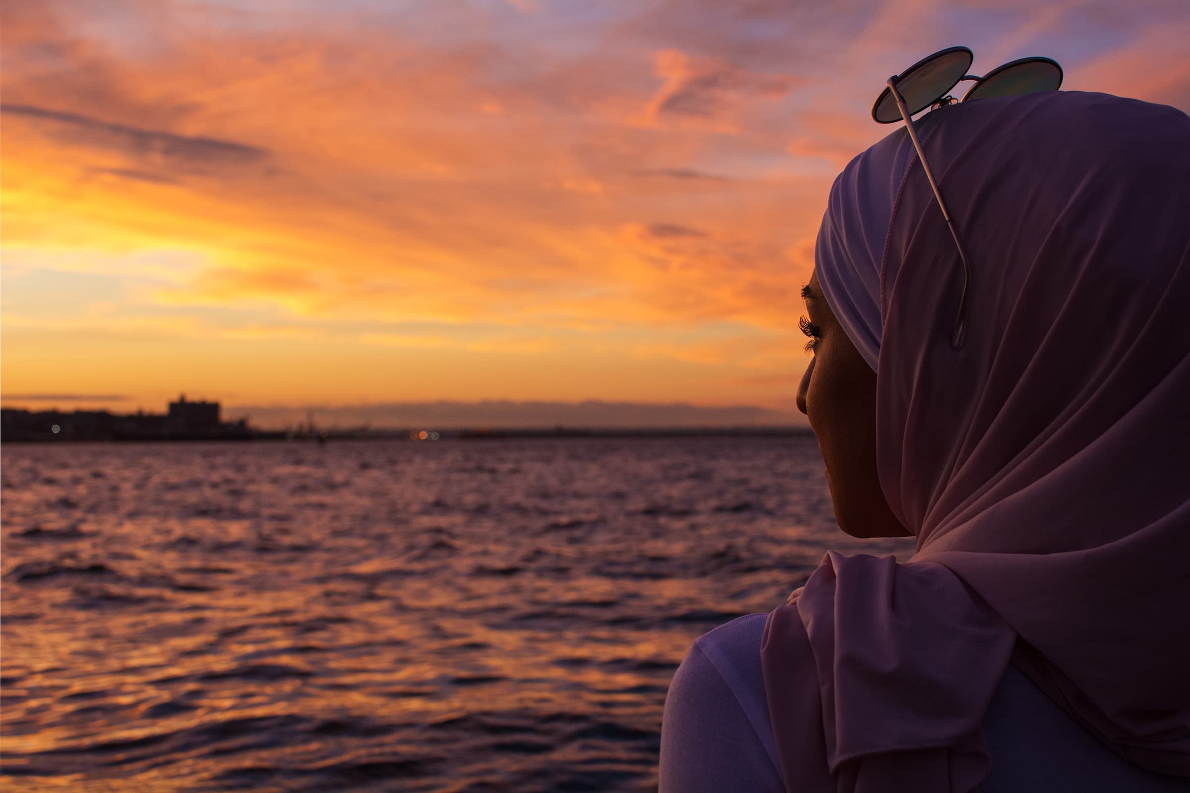 Waterfront portrait of a woman in a lavender hijab at sunset, photographed with a dramatic Tampa Bay sky and warm light.