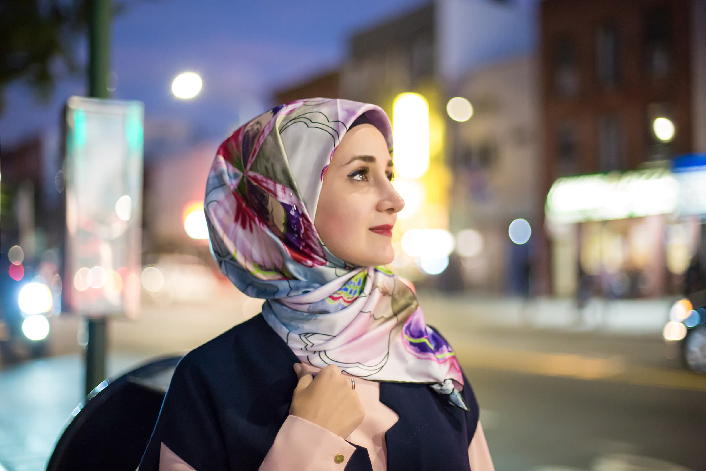 Nighttime cinematic portrait of a woman in a floral hijab, photographed in Tampa with colorful city lights and bokeh.