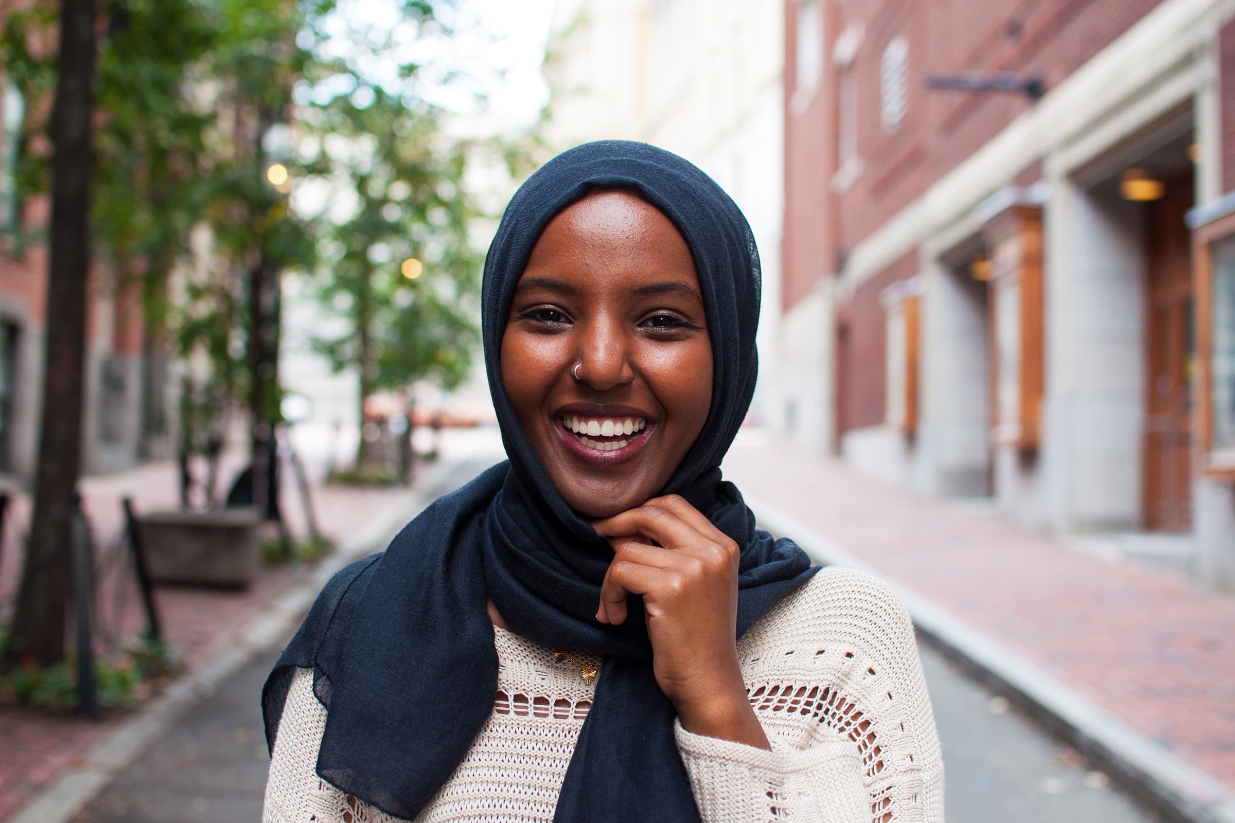 Outdoor portrait of a smiling woman in a blue hijab, photographed on a Tampa city street with soft natural light.