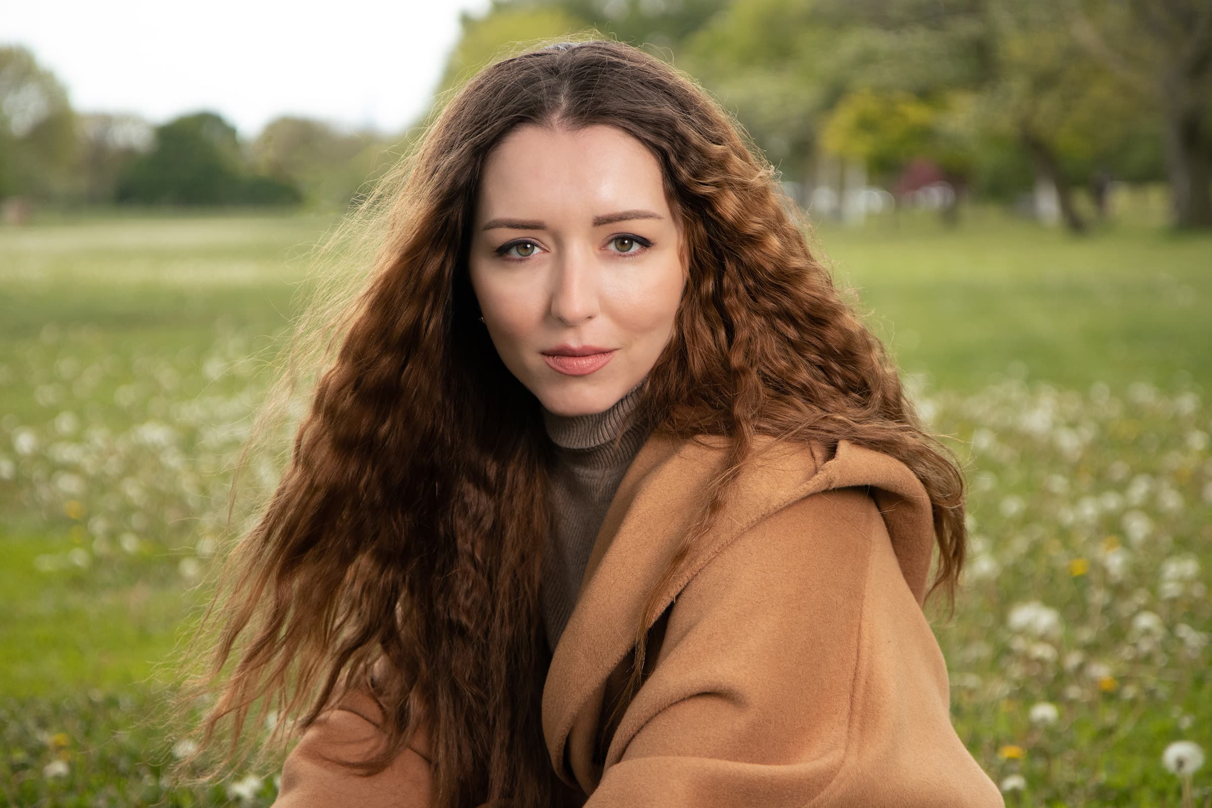 Close-up Tampa portrait of a professional woman in a camel coat, photographed outdoors with soft flash and natural light.