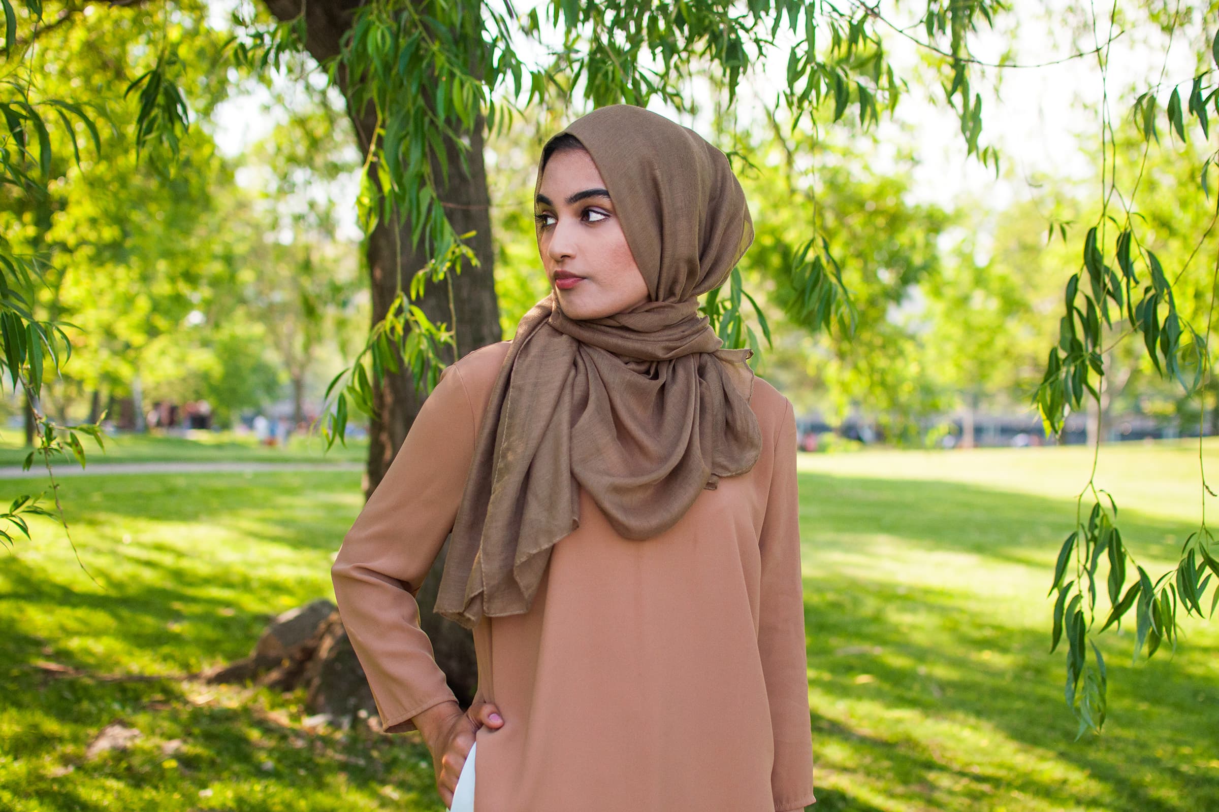 Outdoor portrait of a professional woman in a taupe hijab, photographed in a green Tampa park with soft natural light.