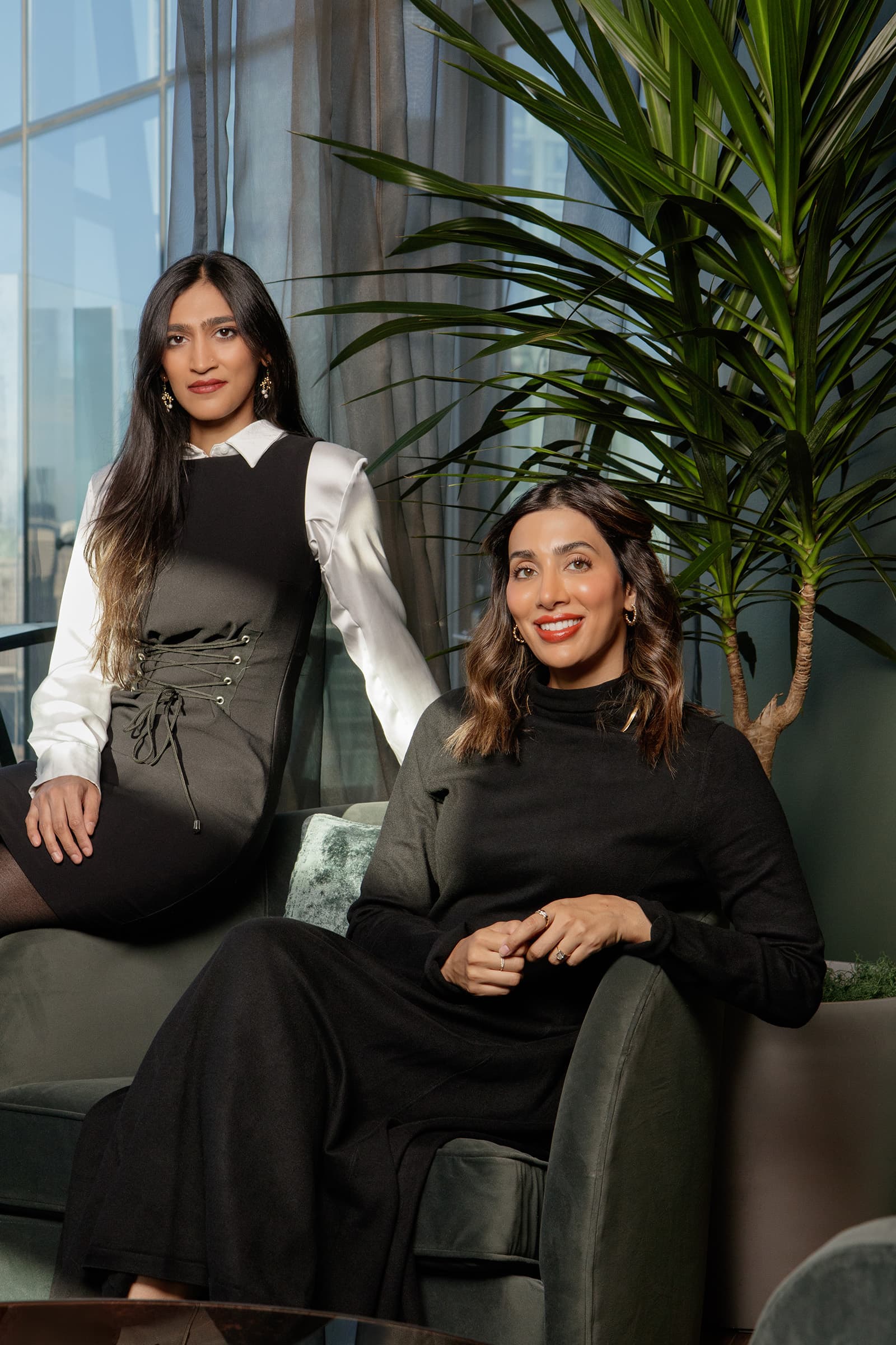 Professional portrait of two women in coordinated business attire seated in a modern Tampa interior with greenery.